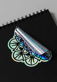 Custom kiss-cut holographic sticker with a 3D pattern on a black notebook, showcasing its printed design.